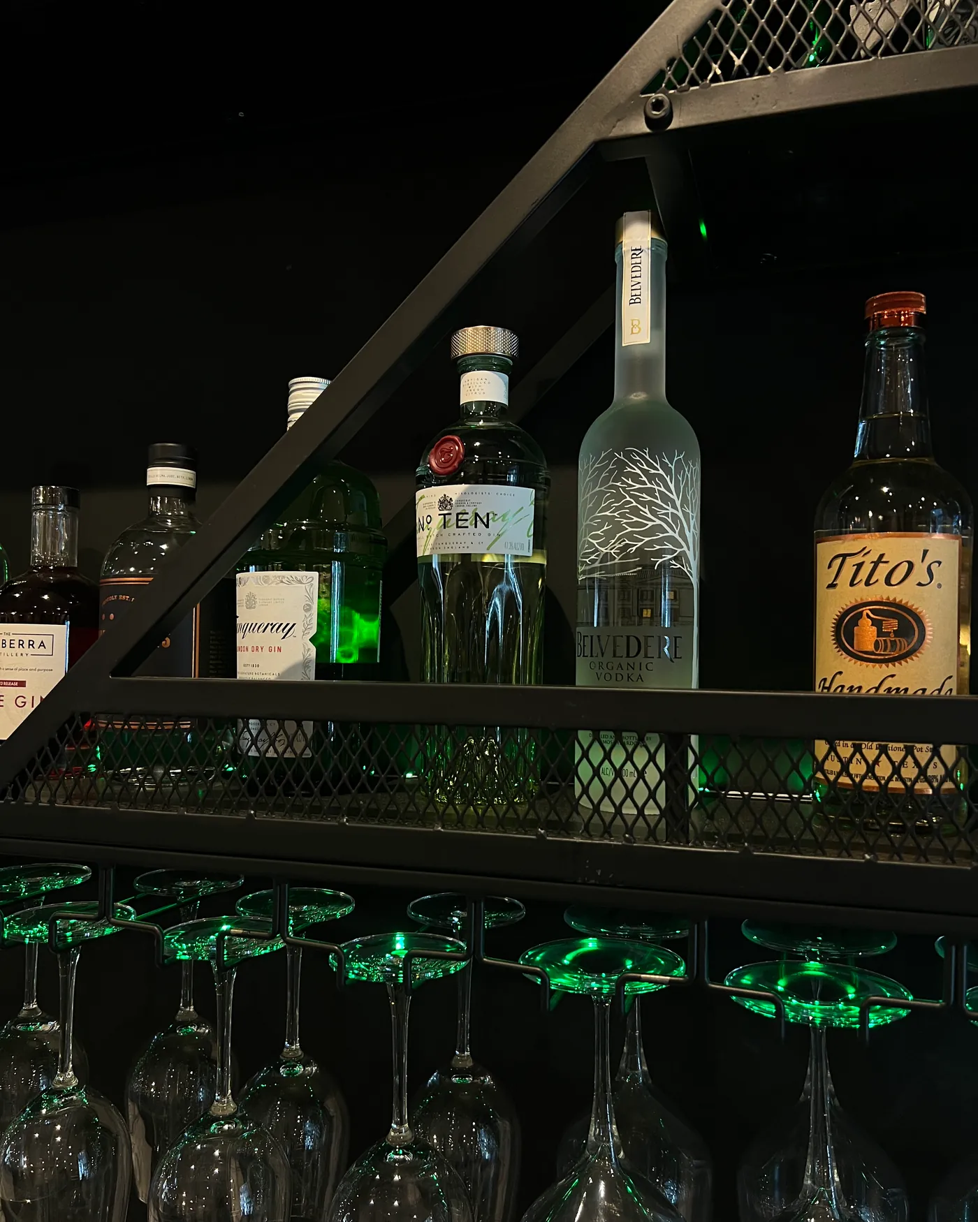 Gin and vodka bottles on the bar shelf above a row of hanging wine glasses