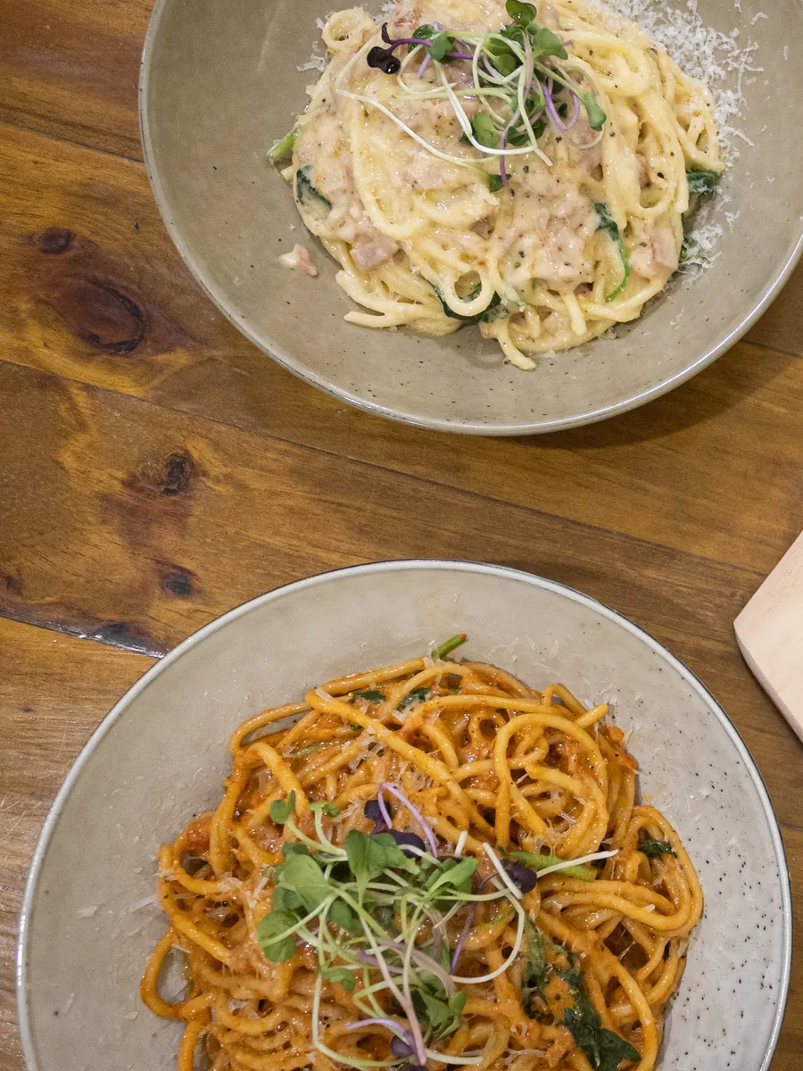 Two bowls of spaghetti, one creamy and one in tomato sauce, topped with micro herbs