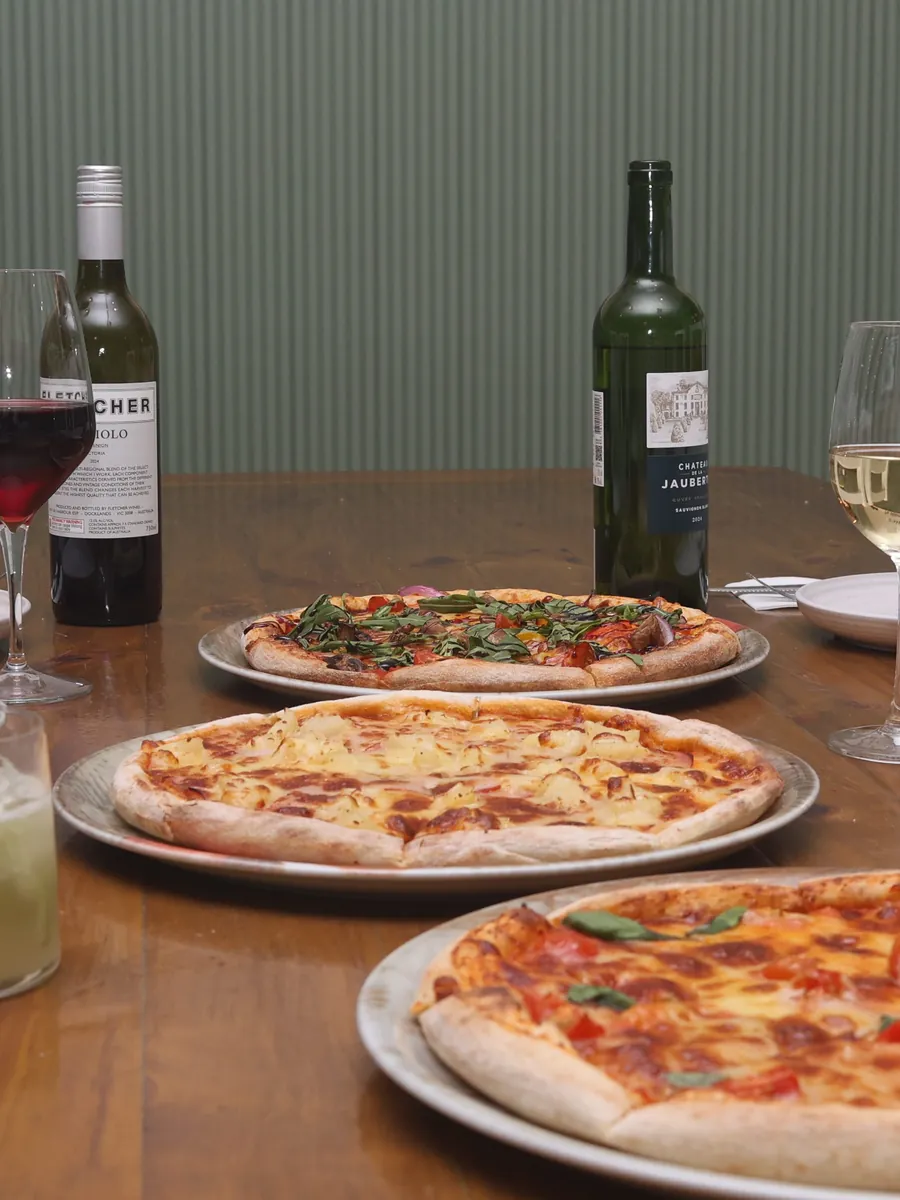 Three pizzas with red and white wine on a wooden table