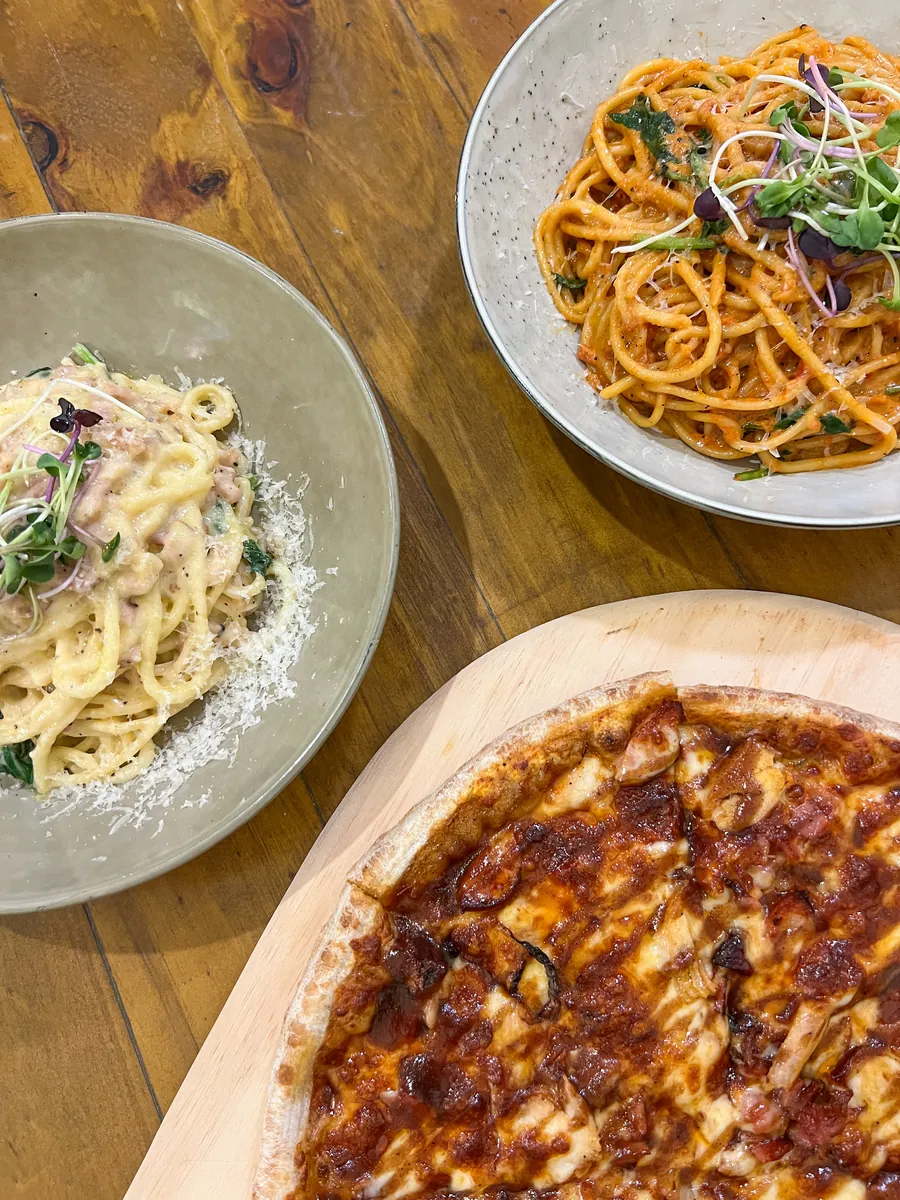 Two bowls of pasta and a pizza on a wooden table, seen from above