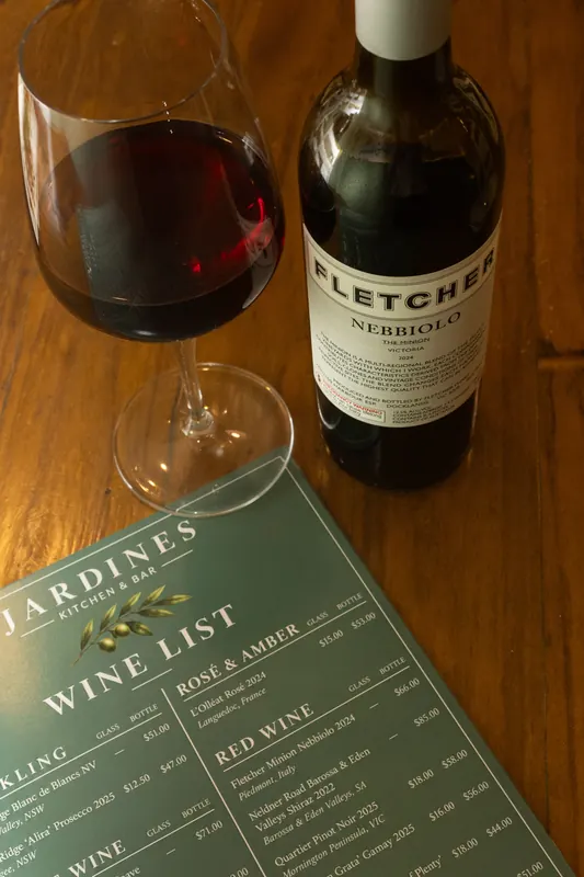 A glass of red wine beside the bottle and the wine list