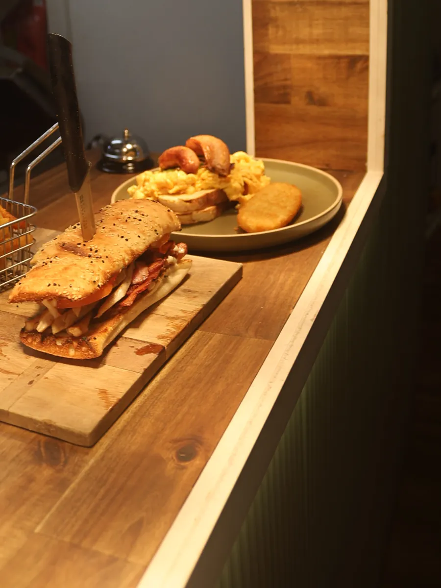 A toasted sandwich on a board with a basket of chips, and a plate of scrambled eggs